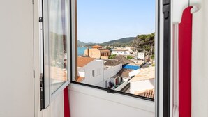 A window view of a coastal town with buildings, a clear sky, and a mountain in the background. - Mar Blava - Apartment In Cala Rajada. Free Wifi (Cala Rajada, Illes Balears)