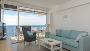 A modern living room with a sofa, a chair, a coffee table, and a TV. There is a balcony with a view of the sea. - Mar Blava - Apartment In Cala Rajada. Free Wifi (Cala Rajada, Illes Balears)