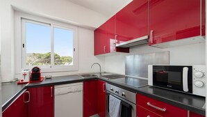 A compact kitchen with red cabinets, a microwave, a dishwasher, and a window with a view of trees. - Mar Blava - Apartment In Cala Rajada. Free Wifi (Cala Rajada, Illes Balears)