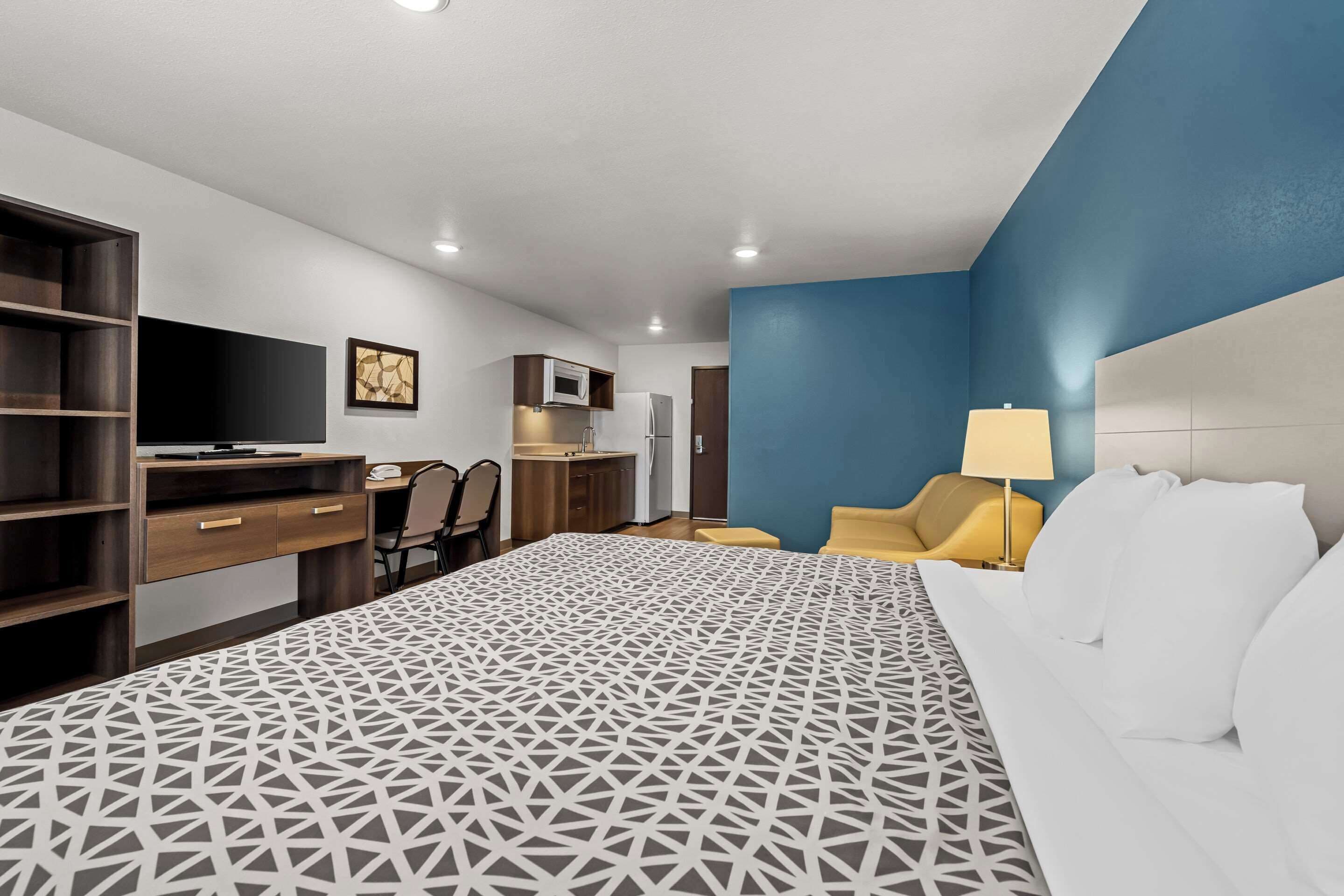 A hotel room with a bed, a desk, a chair, a TV, a microwave, and a small kitchenette.