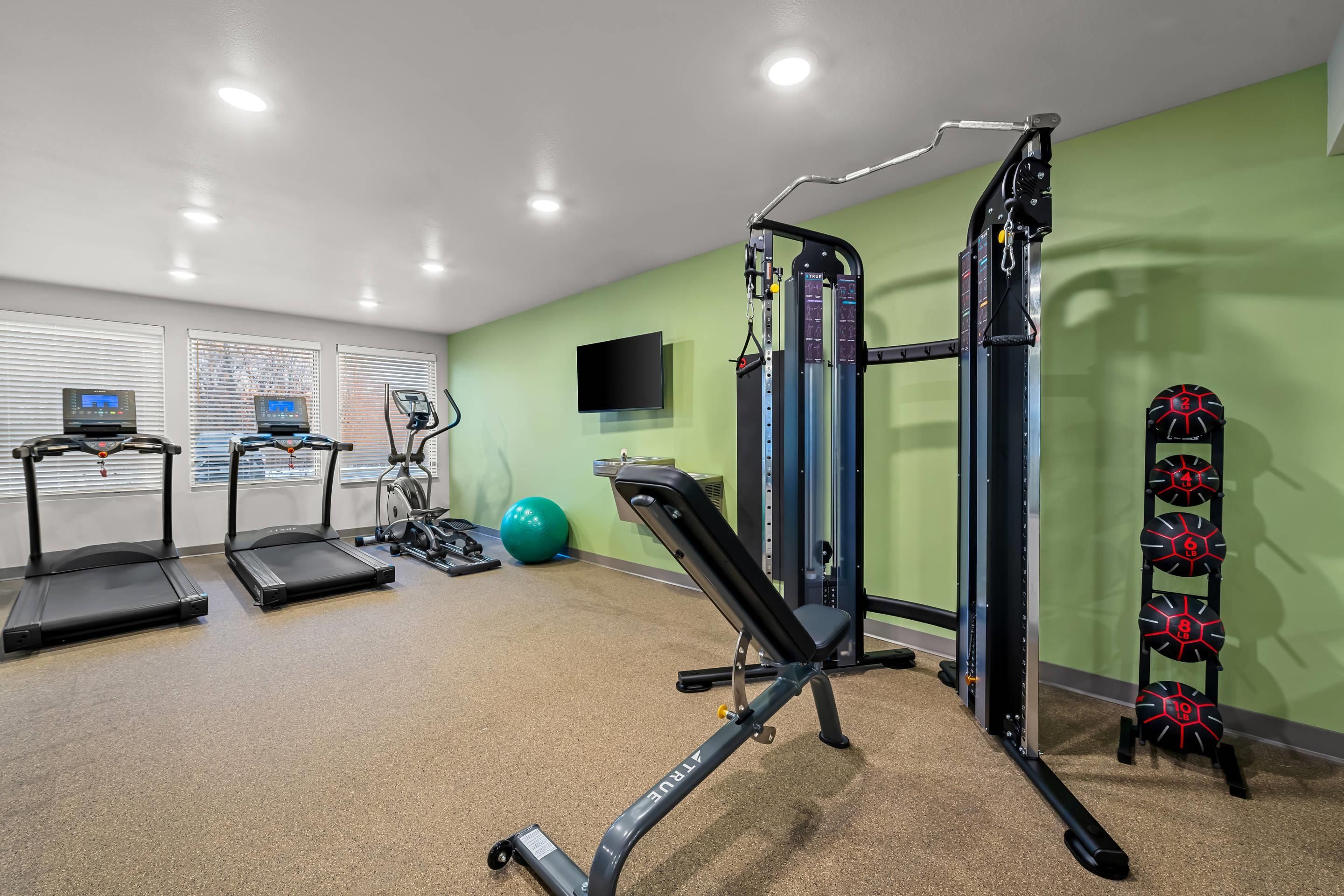 A gym with treadmills, a weight machine, and a wall-mounted TV.