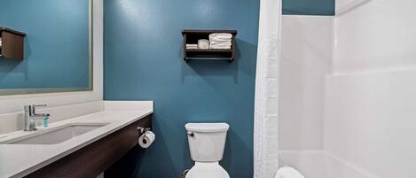 Un baño con inodoro blanco, lavabo con espejo, perchero para toallas y cortina de ducha.