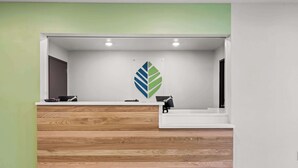 A reception desk with a wooden finish and a white counter. - Woodspring Suites Loves Park Rockford (Loves Park)
