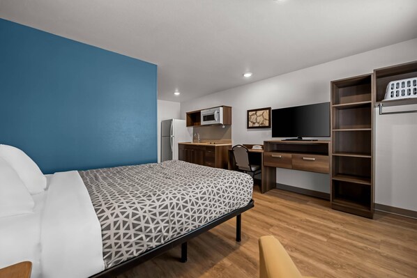 A hotel room with a bed, a desk, a chair, a TV, a wardrobe, and a microwave. - Woodspring Suites Loves Park Rockford (Loves Park)