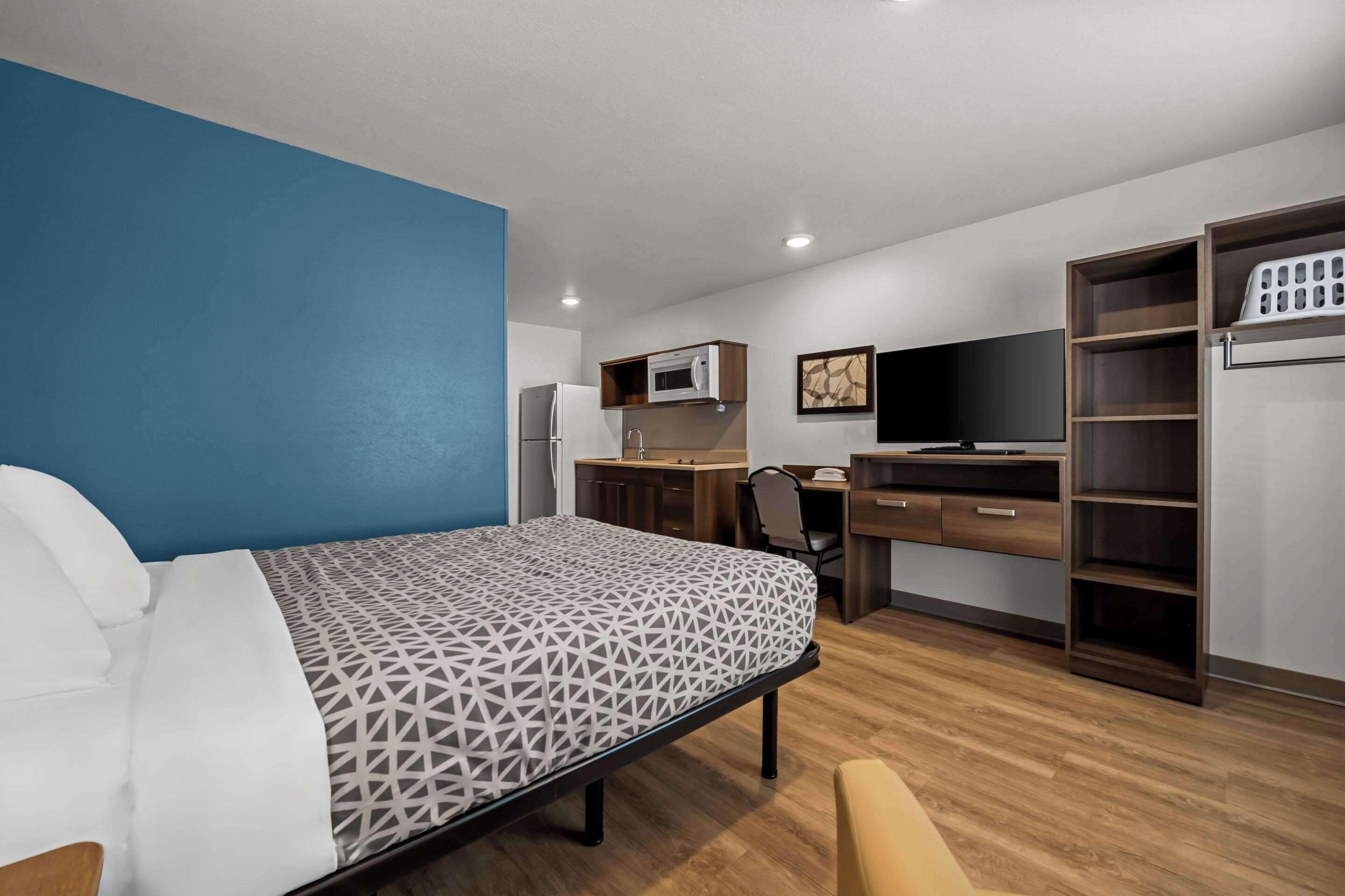 A hotel room with a bed, a desk, a chair, a TV, a microwave, and a wardrobe.