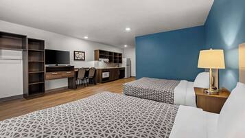 A modern hotel room with a bed, bedside tables, a desk, and a kitchenette.