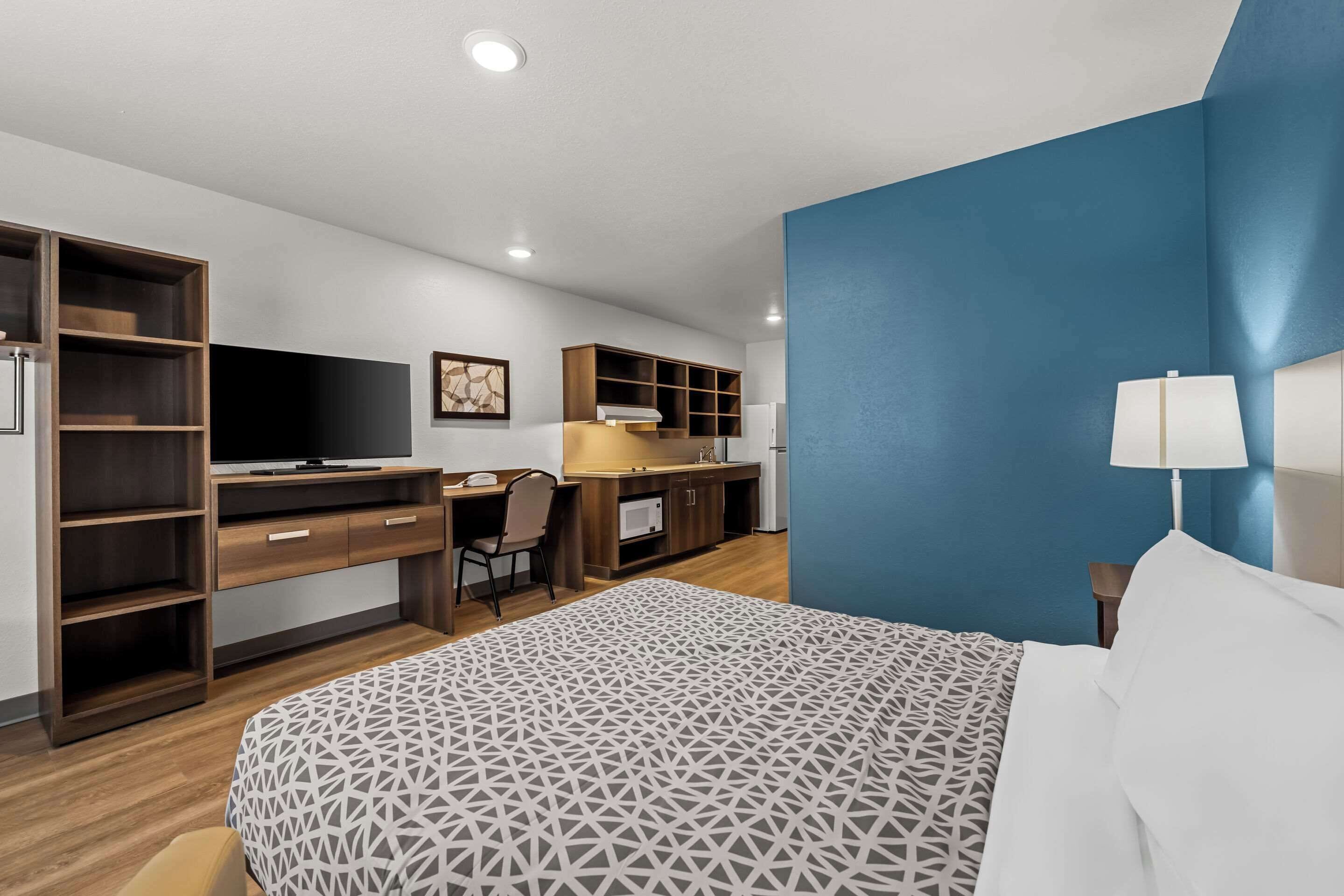 Una habitación de hotel moderna con una cama grande, un escritorio con computadora, televisor y estanterías integradas.