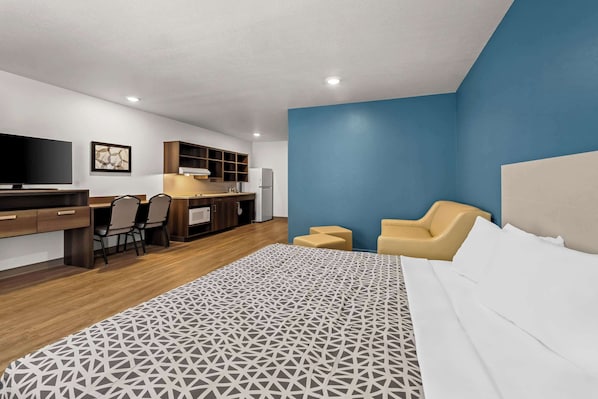 A modern hotel room with a large bed, a desk with a computer, a TV, and a kitchenette. - Woodspring Suites Loves Park Rockford (Loves Park)