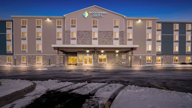 A hotel with a modern facade, multiple entry points, and a parking lot with snow. - Woodspring Suites Loves Park Rockford (Loves Park)