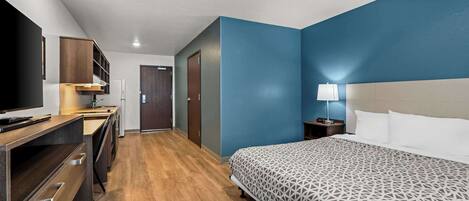 A hotel room with a bed, a desk, a television, and a nightstand with a lamp.