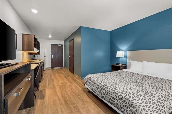 A hotel room with a bed, a desk, a television, and a nightstand with a lamp. - Woodspring Suites Loves Park Rockford (Loves Park)