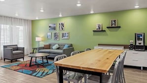 A modern living room with a wooden dining table, grey sofas, and a colorful rug. - Woodspring Suites Loves Park Rockford (Loves Park)