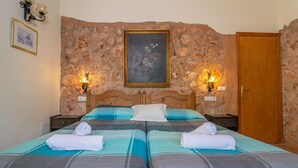 A double bed with two pillows and two towels, a wooden headboard, a stone wall with a painting, and two wall-mounted lamps. - Canaus - Villa With Private Pool In Porreres (Porreres, Illes Balears)