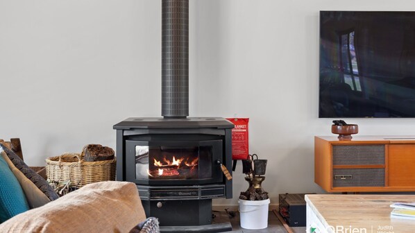 A cozy living room with a wood-burning stove, a television, and a vintage radio.