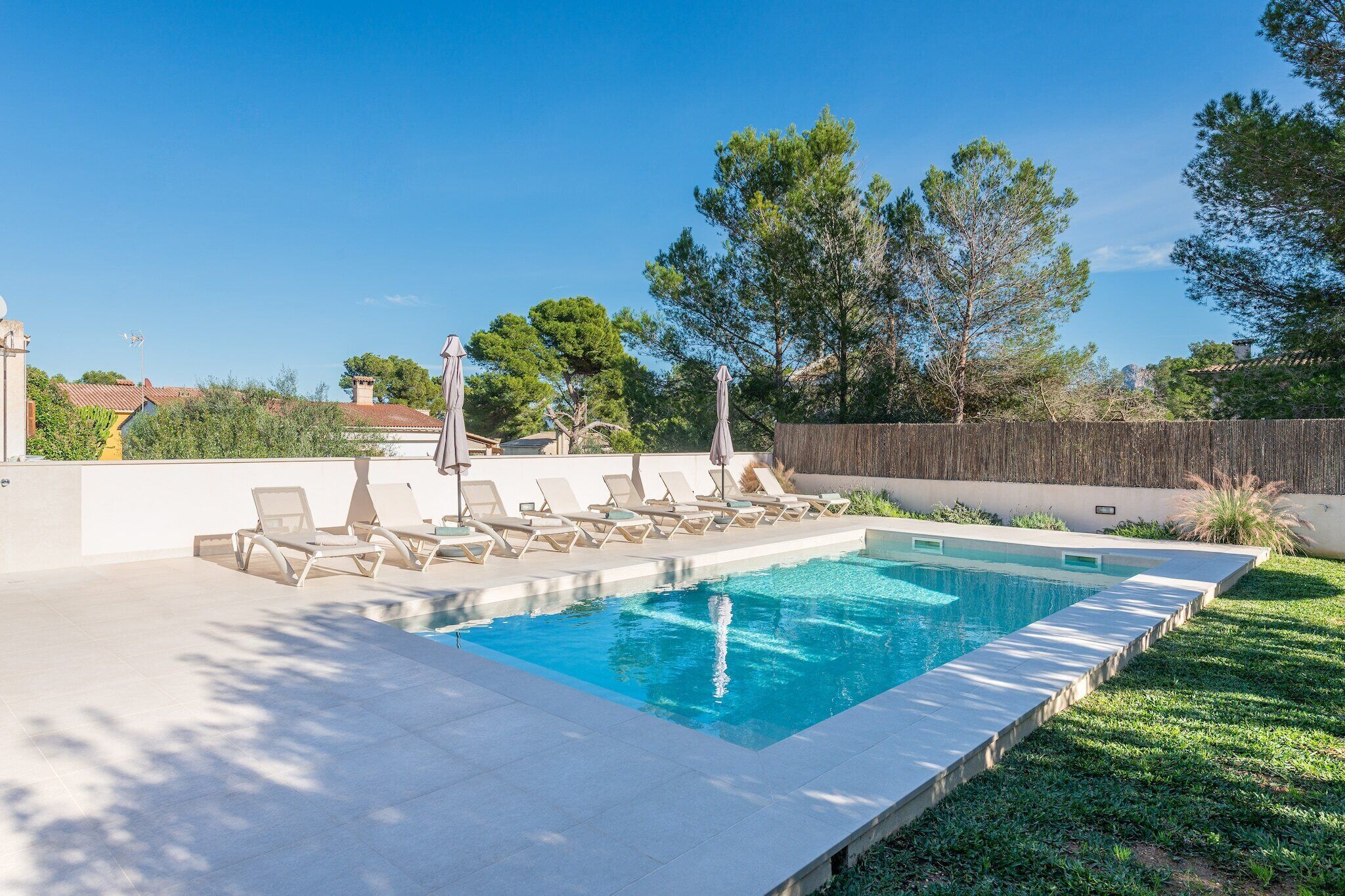Una piscina rectangular con borde de azulejos, rodeada de césped y una valla de madera.