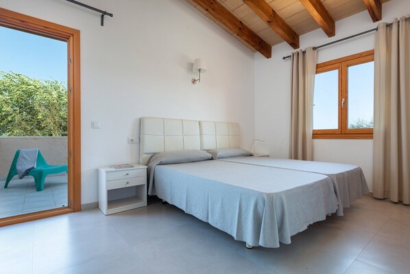 A bedroom with a bed, a nightstand, a window with curtains, and a view of greenery outside.