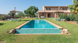 Une piscine bordée de carreaux, entourée d’une pelouse bien entretenue, et une maison avec un toit et des fenêtres recouverts de carreaux.