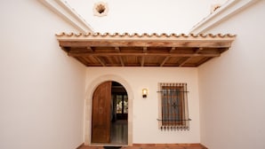 Un patio con suelo de baldosas, una puerta de madera y un ventanal con rejas.