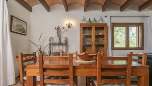 Un coin repas avec une table et des chaises en bois, un buffet contenant de la verrerie et une fenêtre avec des rideaux.