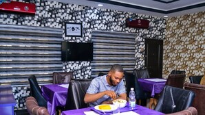 Un hombre cenando en un restaurante con pared estampada y manteles morados.