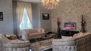 Amplia sala de estar con un sofá grande, dos sillones, una araña, un televisor y una pared de piedra.