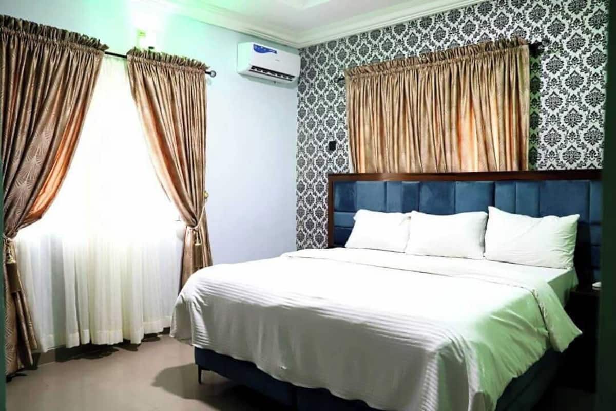 Una camera da letto con un letto, tende, un condizionatore e carta da parati fantasia.