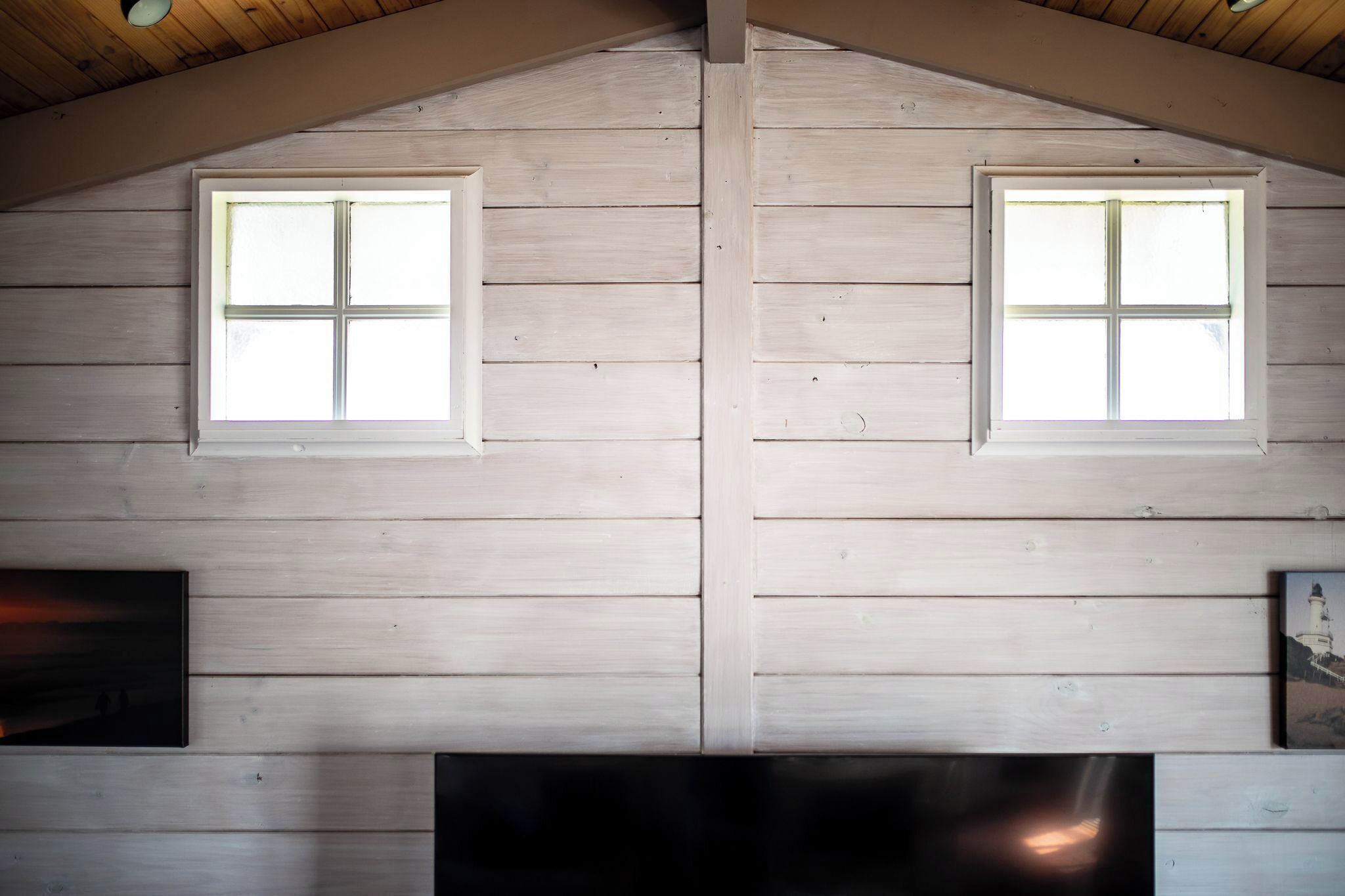 A room with two windows, wooden walls, and a flat-screen TV.
