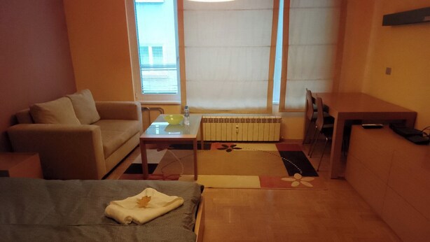 Habitació d'hotel amb un llit, un sofà, una taula petita amb una ampolla d'aigua, un radiador i un escriptori amb una cadira.