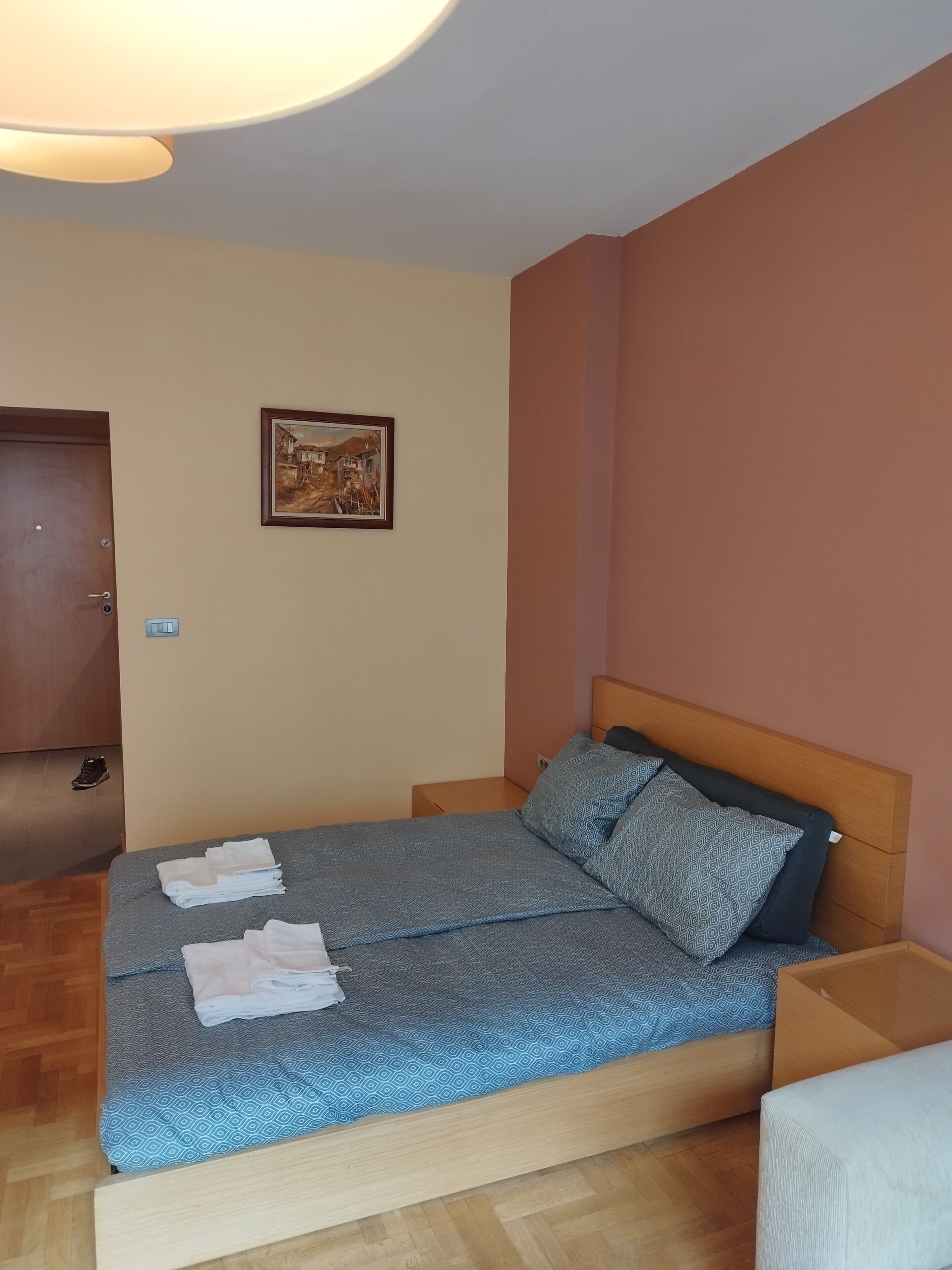 A neatly arranged bedroom with a bed, a bedside table, a wall-mounted picture, and a door.