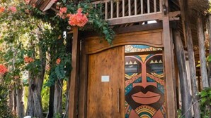 Une structure en bois surmontée d’un toit de chaume, une porte ornée d’une fresque colorée et une entrée pavée de pierres.