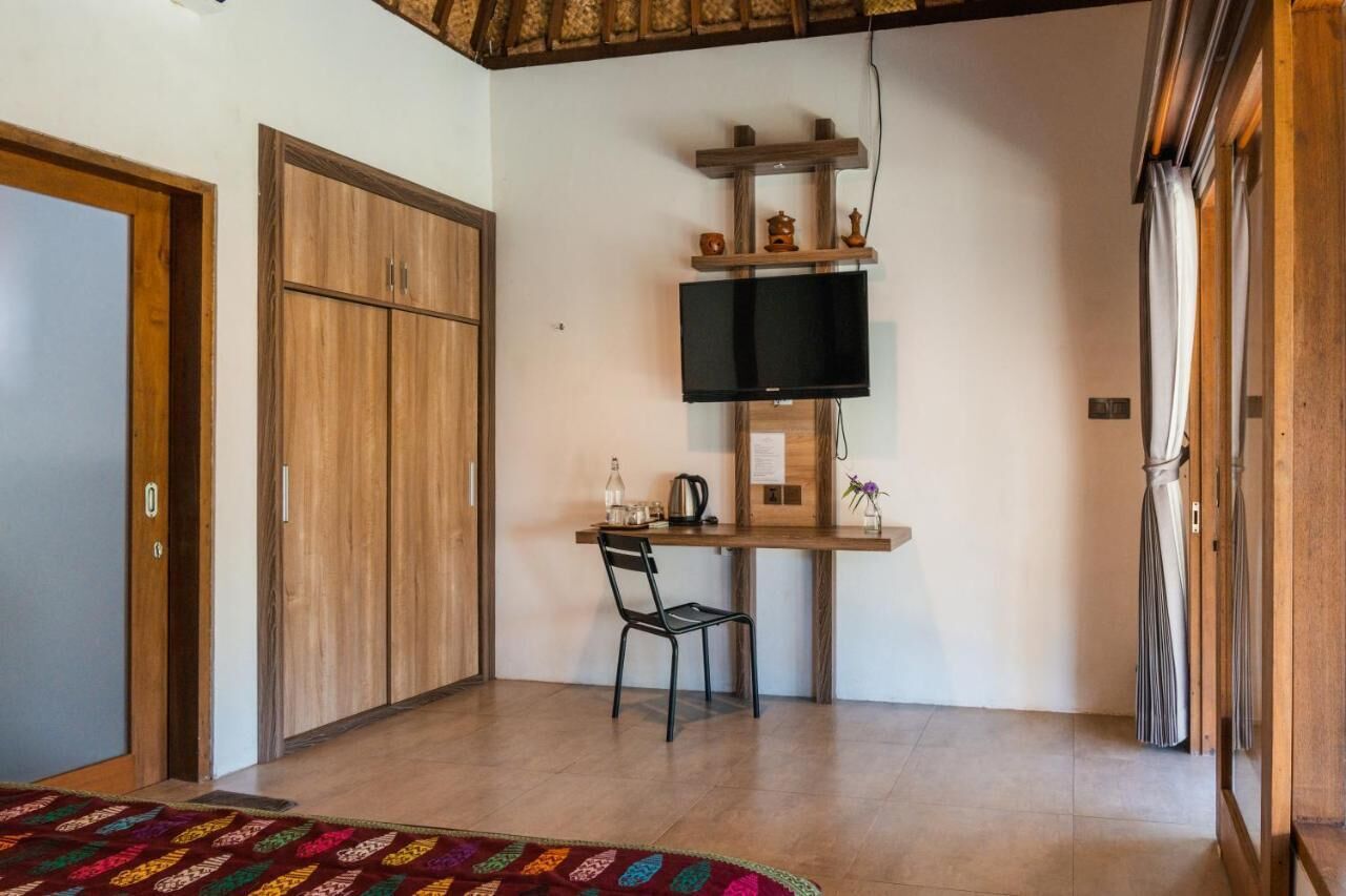 Ein Zimmer mit einem Holzschrank, einem Schreibtisch mit Flachbildfernseher, einem Sessel und einem gemusterten Teppich.