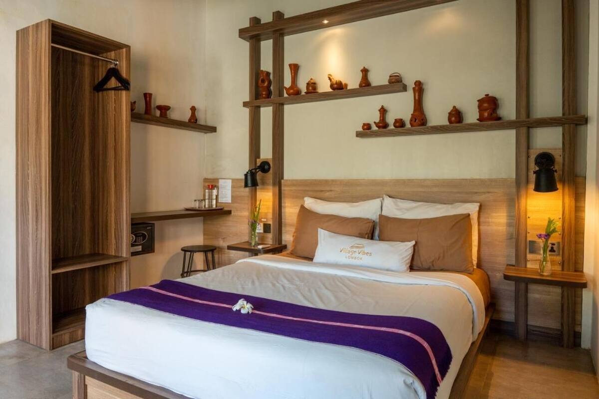 Une chambre d’hôtel avec un lit en bois, une table de chevet avec une lampe, une étagère avec des objets en céramique et une armoire.