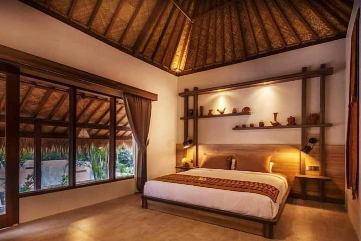 Une chambre à coucher avec un lit, une fenêtre et une étagère où sont disposés des objets décoratifs.