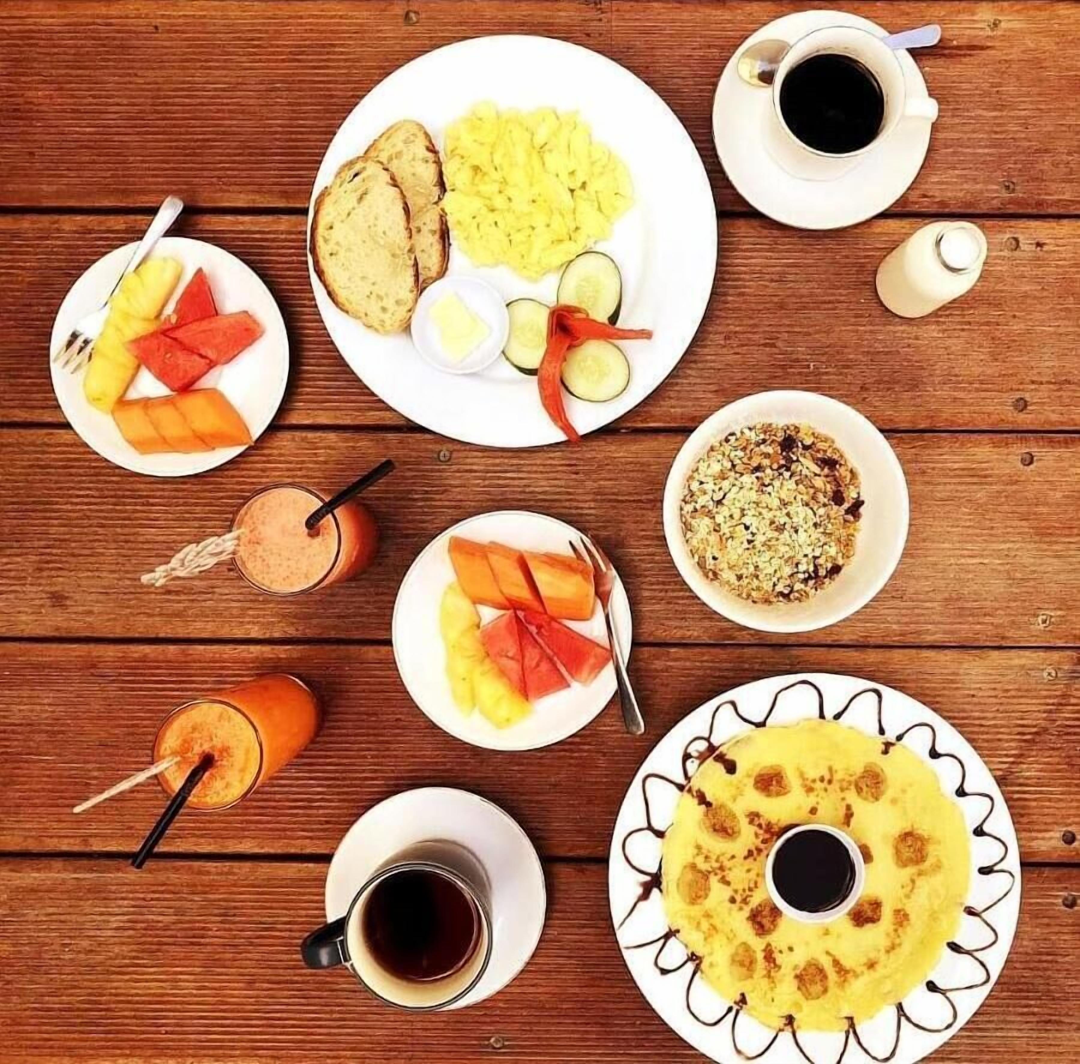 Una mesa de madera con diversos alimentos para el desayuno, como tostadas, huevos revueltos, fruta y bebidas.