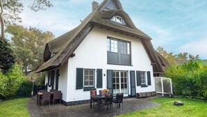 Une maison traditionnelle avec un toit de chaume très pentu, des murs blancs et des volets sombres.