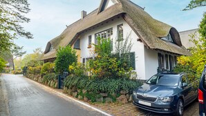 Une maison traditionnelle à toit de chaume, avec une allée pavée et une voiture garée.