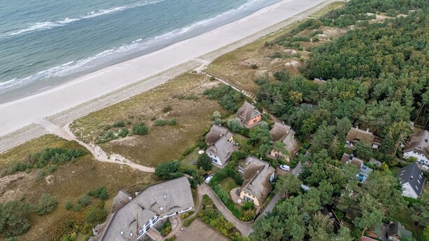 Vue aérienne d’une zone côtière avec une plage, des maisons et une végétation luxuriante.