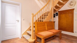 Un escalier avec des rampes et des marches en bois, un banc en bois avec des coussins, une porte blanche et un meuble fixé au mur.