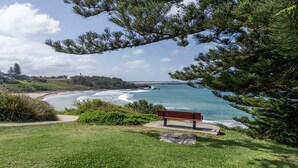 A coastal landscape with a bench overlooking the sea, grassy areas, and a distant lighthouse. - Craigmore On The Beach Unit 11 - Lifestyle Yamba (YAMBA)