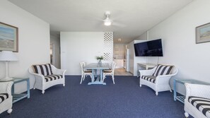 A room with a dining table, two chairs, a TV mounted on the wall, and a ceiling fan. - Craigmore On The Beach Unit 11 - Lifestyle Yamba (YAMBA)