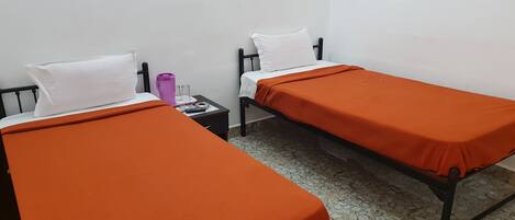 Two single beds with orange bedding, white pillows, and a small bedside table with a purple water bottle and glasses.