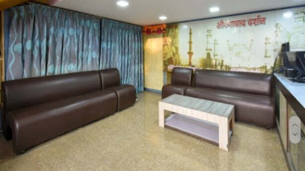 Zona de recepción con dos sofás marrones, una mesa de centro blanca y una pared con un cartel.