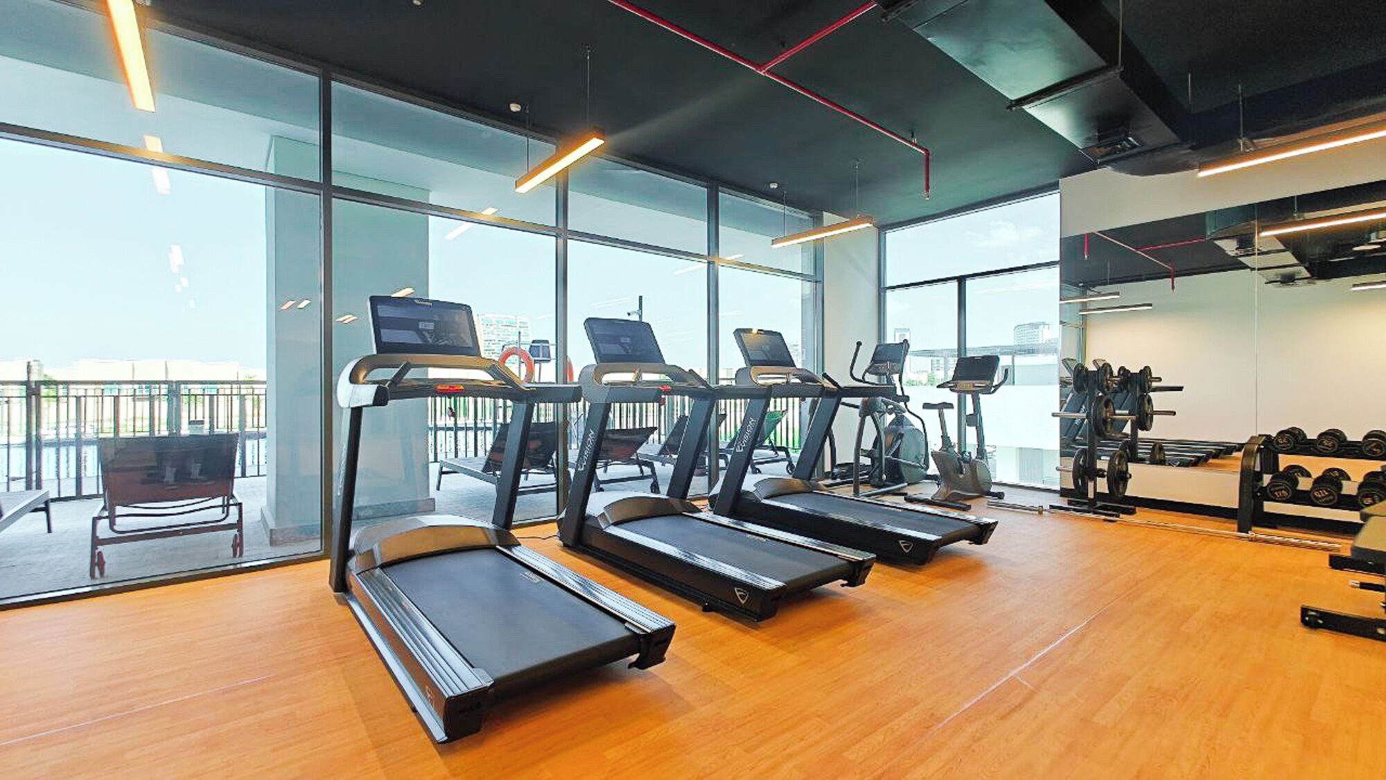 A gym with treadmills, weight machines, and a view of the city through large windows.