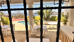 A covered outdoor area with a pool, white tables and chairs, and a view of the ocean.