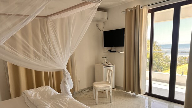 A hotel room with a bed, a desk, a chair, a TV, and a view of the outdoors.