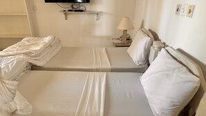 A twin bed with white linens, a bedside table with a lamp, and a wall-mounted TV.