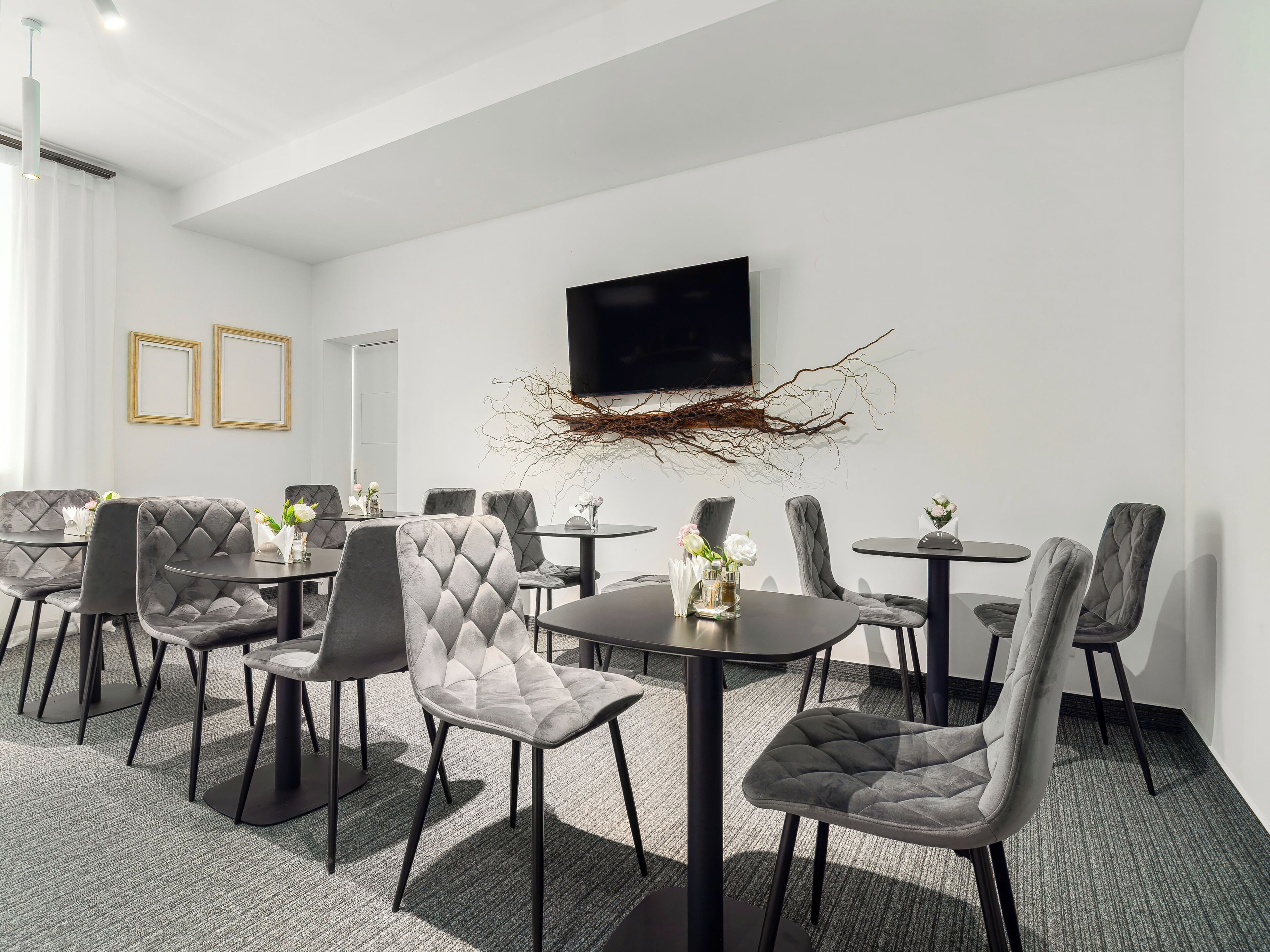 A modern dining area with tufted chairs and round tables, a flat-screen TV mounted on the wall, and a decorative branch piece above the TV.