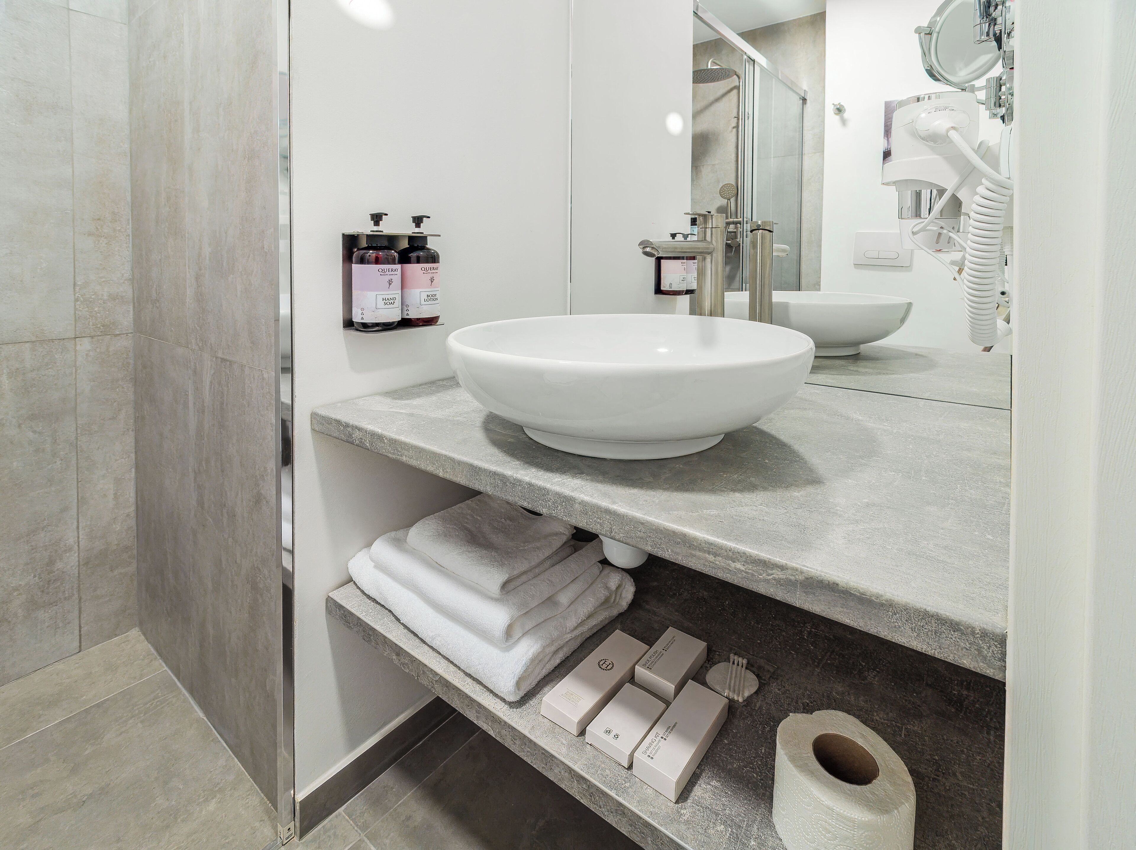 A modern bathroom with a large white sink, a glass shower enclosure, and neatly folded towels on a shelf.