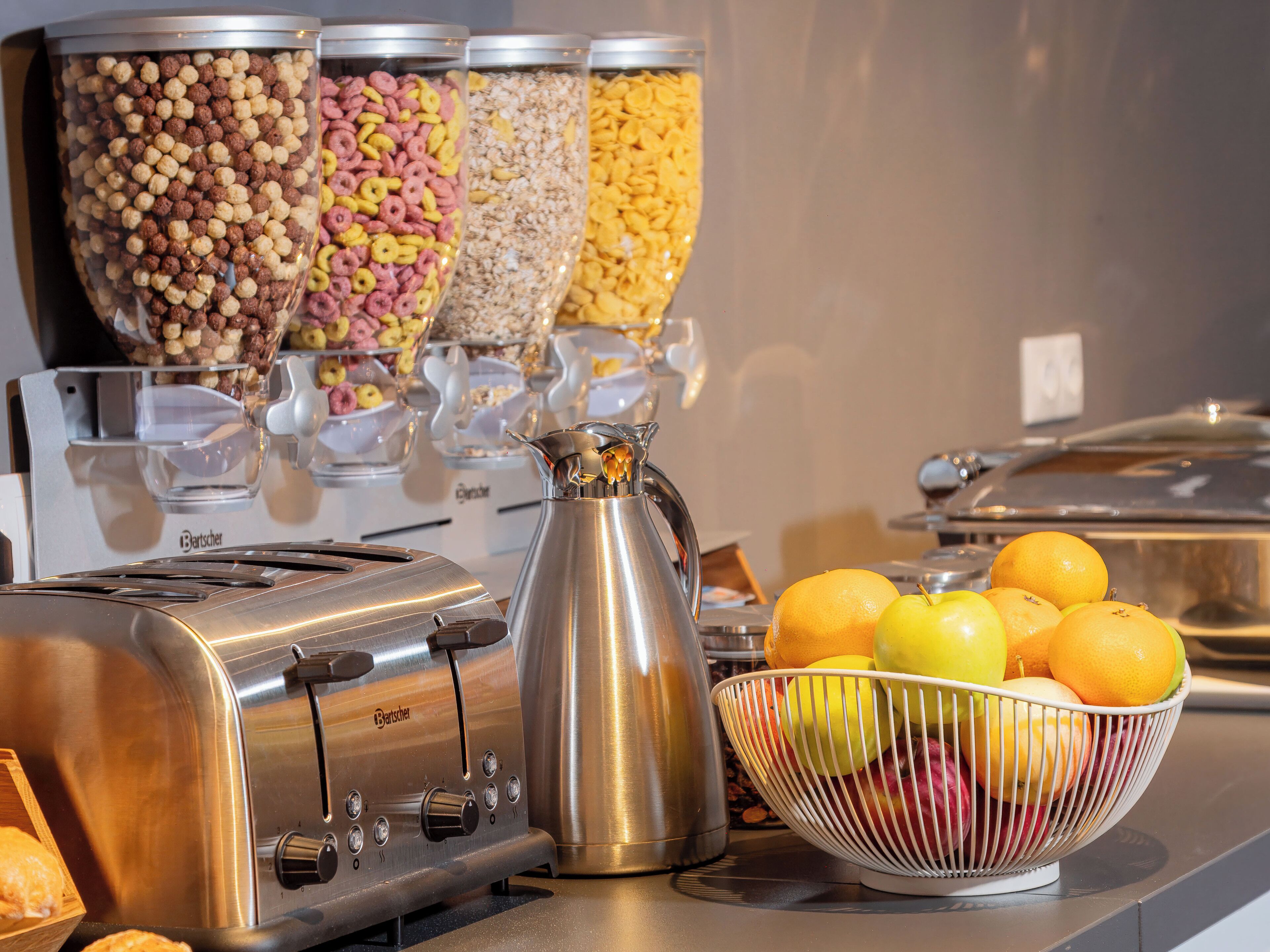 A buffet setup with various food containers, a coffee pot, and a fruit bowl.