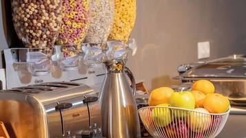 A buffet setup with various food containers, a coffee pot, and a fruit bowl.